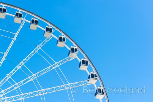 Cabins of the 'La Grande Roue de Montréal' Ferris wheel against a clear blue sky, with the waxing moon in the distance