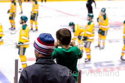 A young boy is held up to see the Clarkson Golden Knights hockey team over the glass at the ECAC Hockey tournament