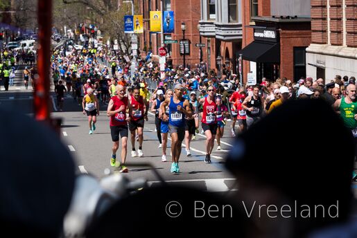 A pack of runners approaching the final turn in the 126th Boston Marathon, framed by spectators looking on