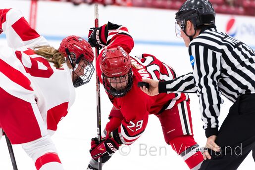 Women's hockey face-off between RPI and Boston University, with both players eyeing the puck in the linesman's hand