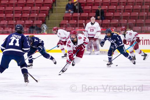 A Harvard women's hockey forward avoids Yale players as she skates the puck into the opposing zone