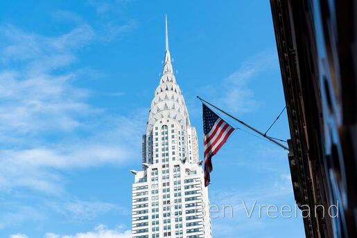 An American flag flown stories below is juxtaposed with the crown of the Chrysler Building on a cloudy day